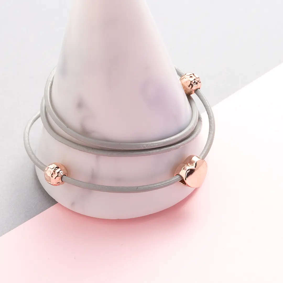 An close image of a bracelet on a marble plinth, with a grey and pink backdrop.