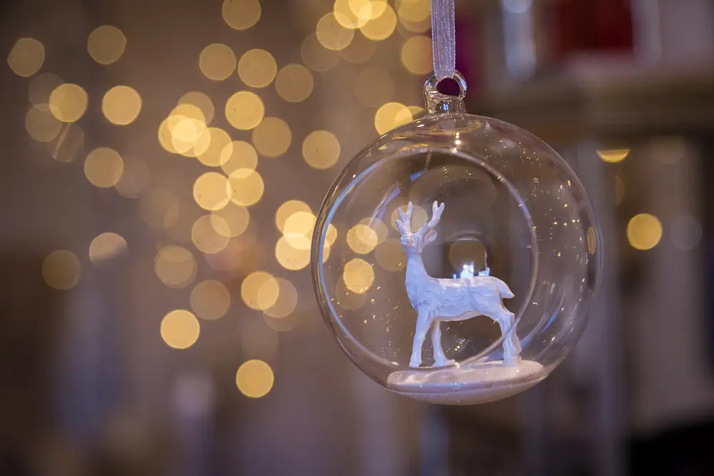 A close up image of a reindeer Christmas decoration hanging on a tree, with blurry lights in the background